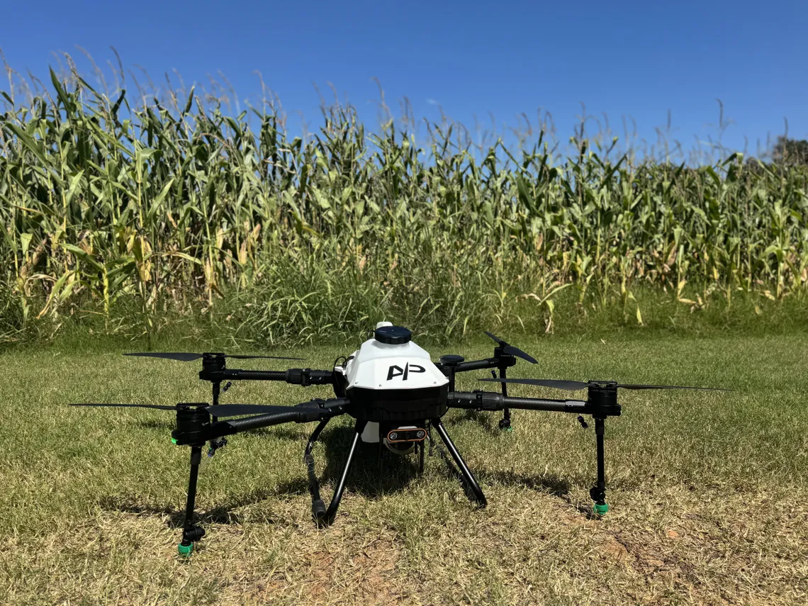 American Prime spray multirotor staged on the ground at the edge of a corn field