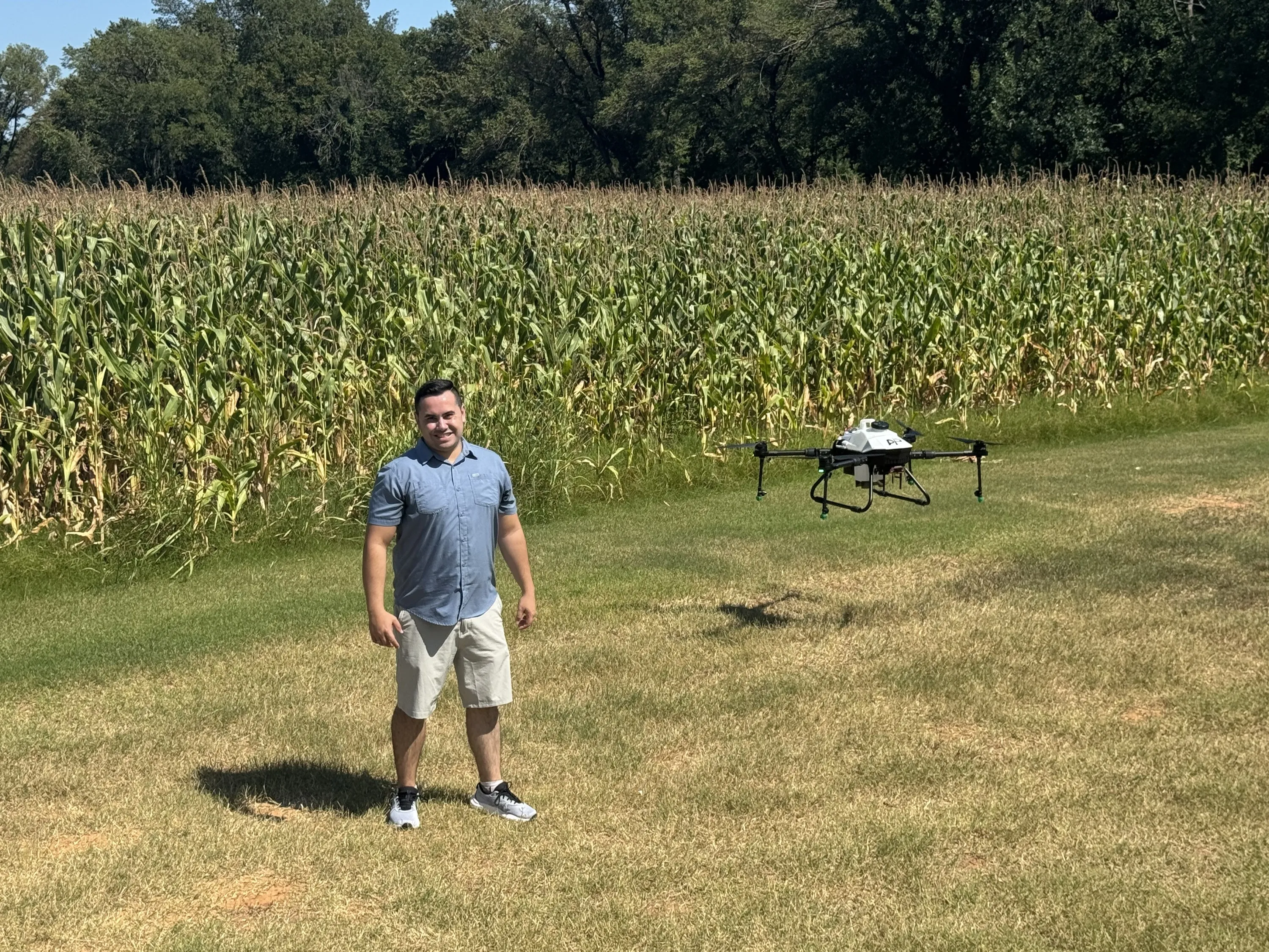 Founder Jorge Celis standing beside a corn field with an AP spray drone hovering behind him